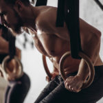 Group of young male and female adults doing pull ups on bar in cross fit training gym