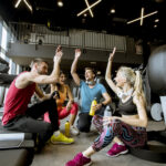 Friends in sportswear talking and laughing together while sitting on the floor of a gym after a workout