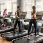 Group of four people running on treadmills in fitness gym